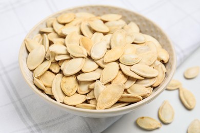Photo of Bowl with pumpkin seeds on light table, closeup