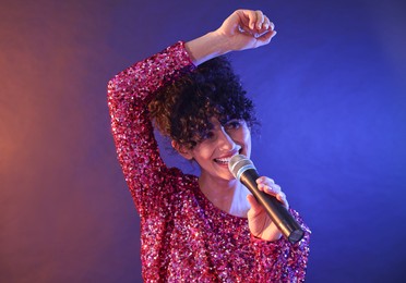 Beautiful young woman with microphone singing on color background in neon lights