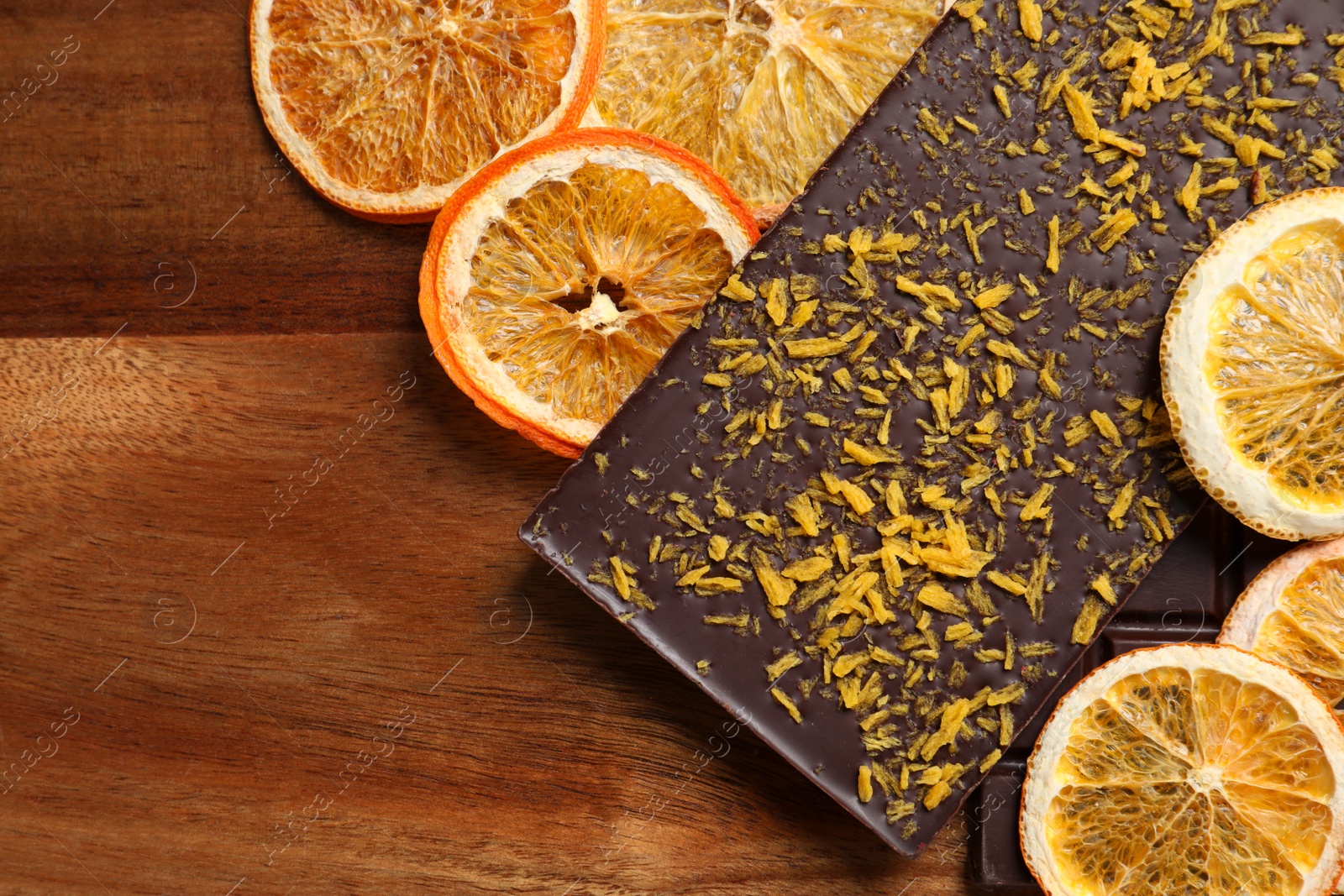 Photo of Chocolate bars with freeze dried orange on wooden table, top view. Space for text