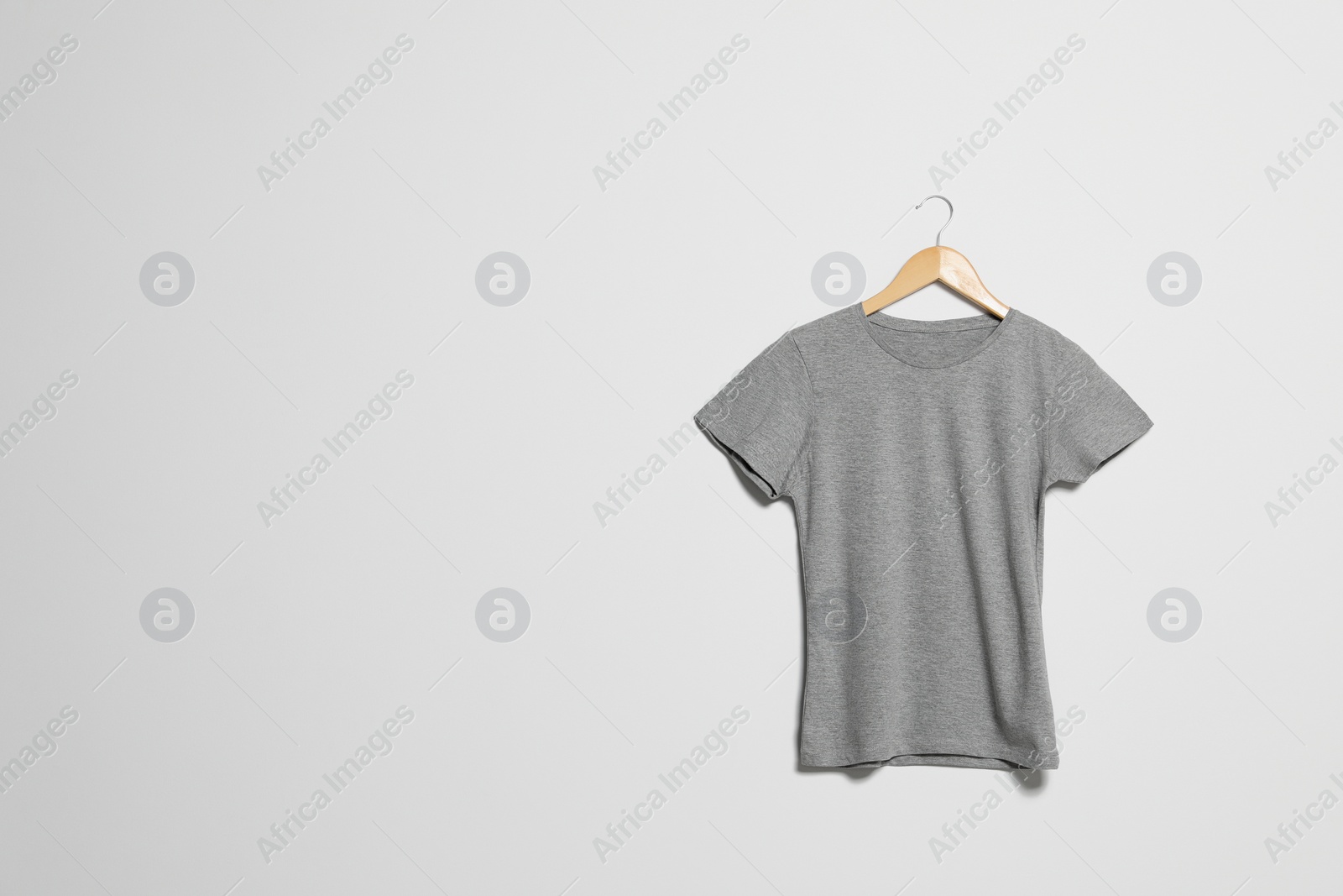 Photo of Hanger with grey t-shirt on light wall. Mockup for design