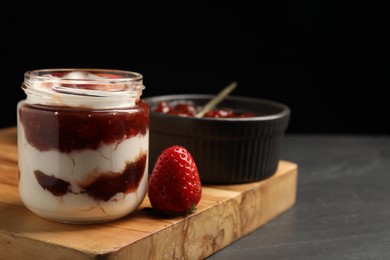 Photo of Tasty yoghurt with jam and strawberries on black table, closeup. Space for text