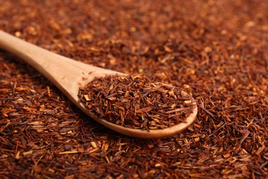 Photo of Heap of dry rooibos tea leaves with wooden spoon, closeup view