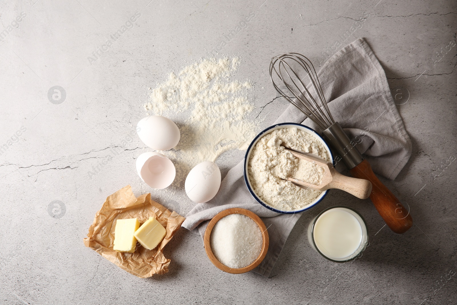 Photo of Different ingredients for dough and whisk on light textured table, flat lay