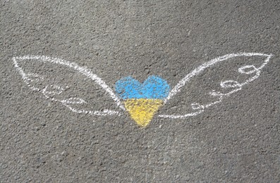 Heart and wings drawn with blue and yellow chalks on asphalt outdoors, top view