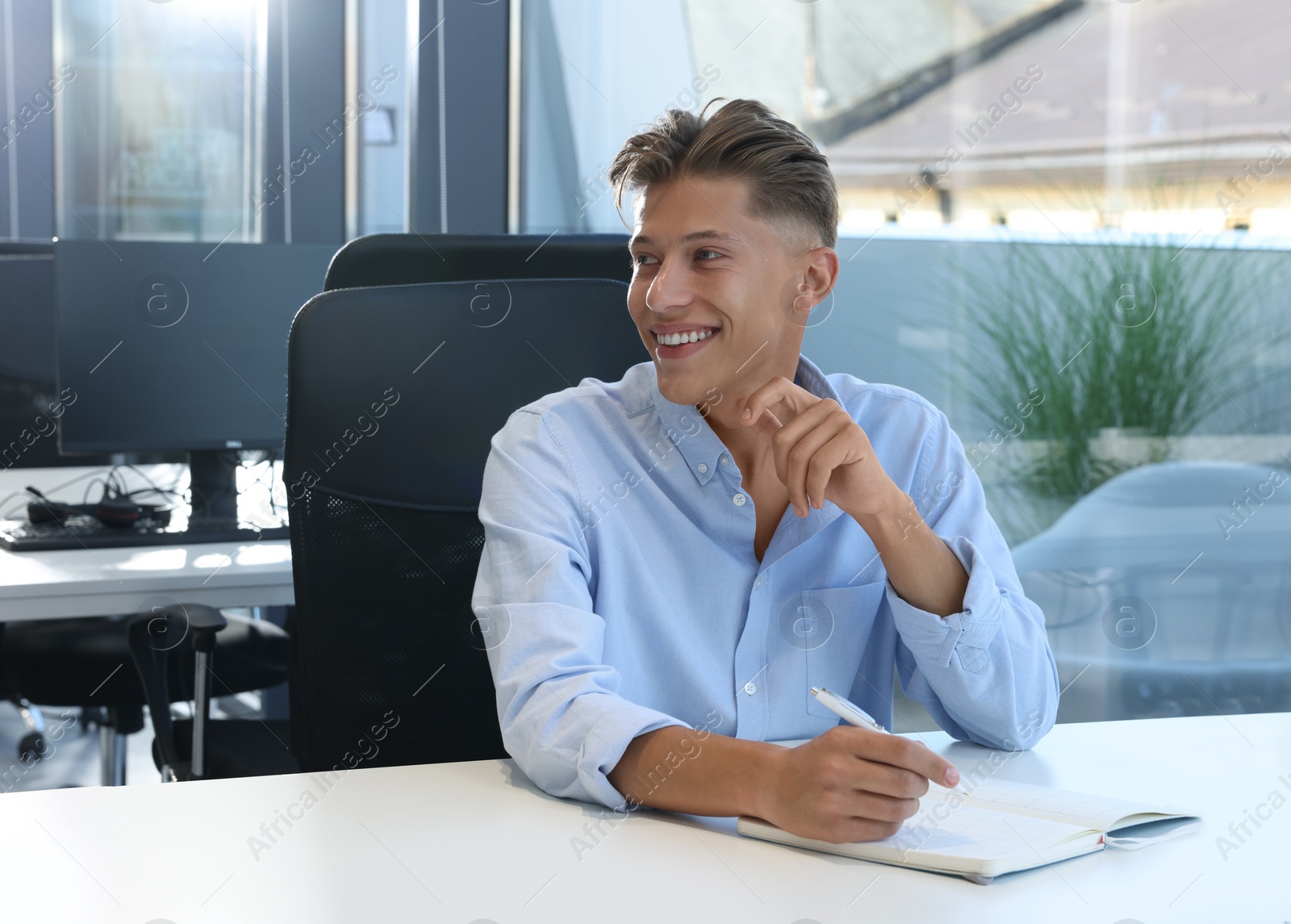 Photo of Happy man taking notes at white desk in open plan office, space for text