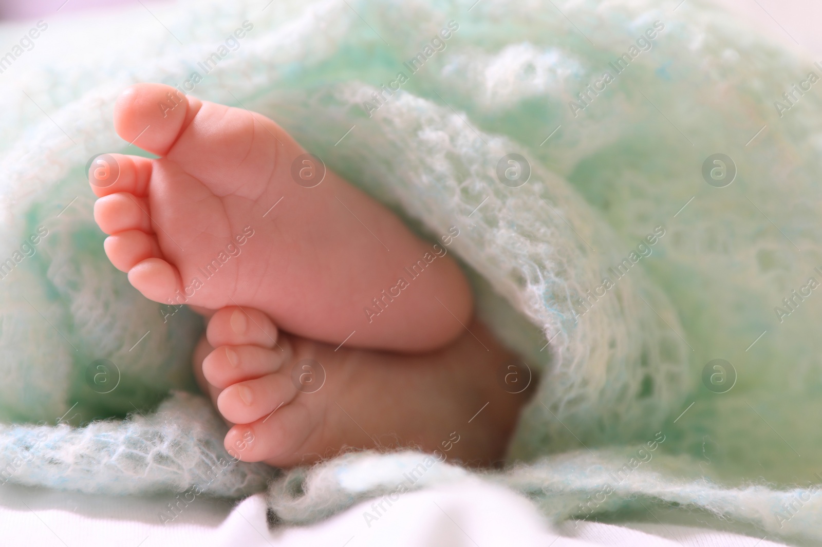 Photo of Cute newborn baby covered in turquoise crocheted plaid on bed, closeup of legs