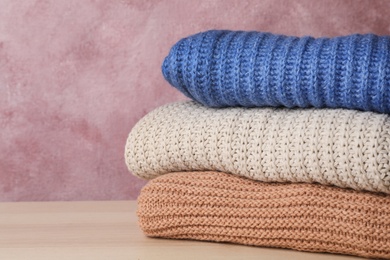 Photo of Stack of folded knitted sweaters on table. Space for text