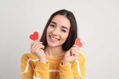Photo of Portrait of beautiful young woman with paper hearts on light background