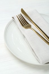 Stylish ceramic plate, cutlery and napkin on white wooden table, closeup