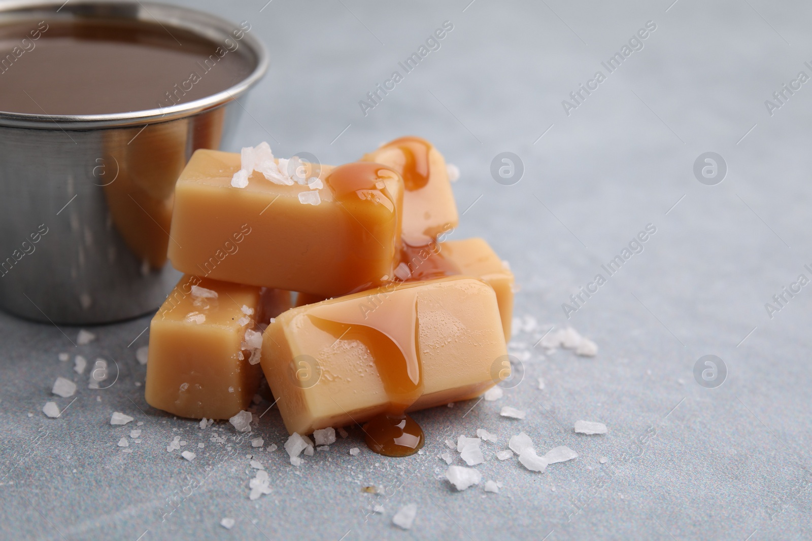 Photo of Yummy caramel candies, sauce and sea salt on grey table, closeup. Space for text