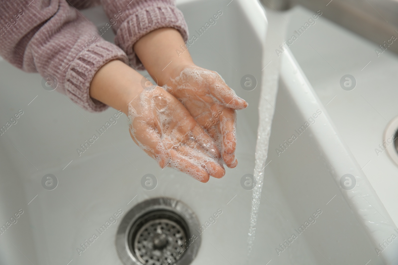 Photo of Little girl washing hands with liquid soap, closeup