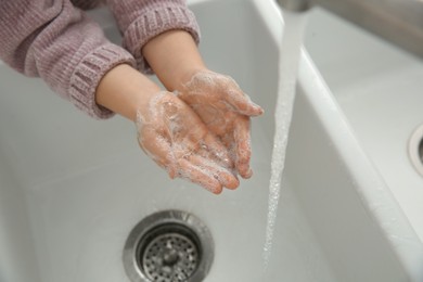 Photo of Little girl washing hands with liquid soap, closeup