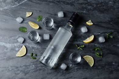Photo of Bottle of vodka, shot glasses, lemon, mint and ice on black marble table, flat lay