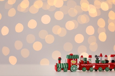 Photo of Toy train on white table against Christmas lights. Space for text