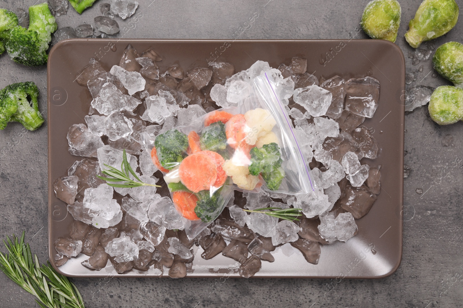 Photo of Mix of different frozen vegetables with ice on grey table, flat lay