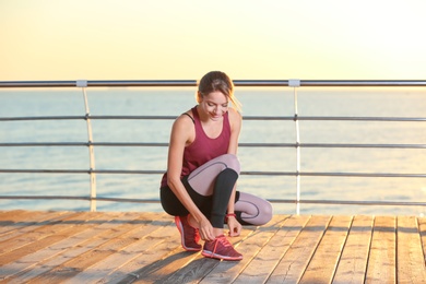 Photo of Young woman tying shoelaces on pier. Morning workout