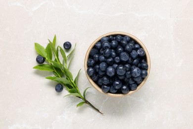 Photo of Bowl of tasty fresh bilberries and green leaves on white table, flat lay