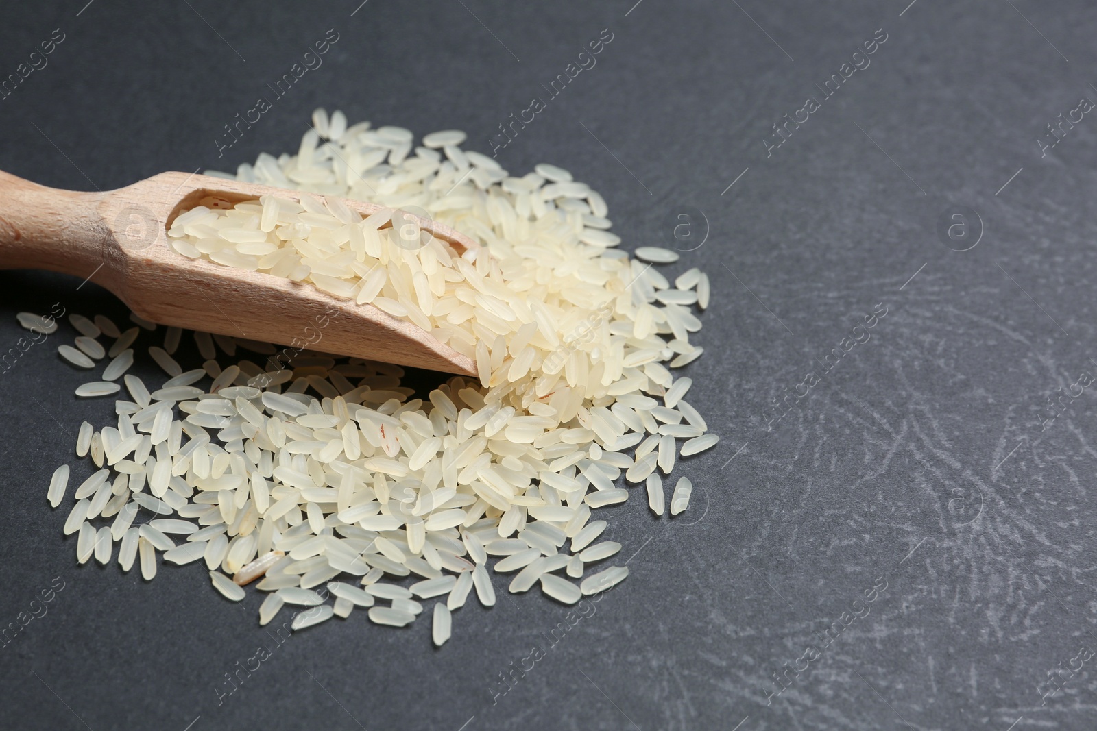 Photo of Parboiled rice and wooden scoop on grey table, closeup