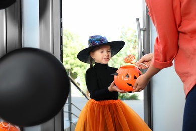 Photo of Cute little girl dressed as witch trick-or-treating at doorway. Halloween tradition