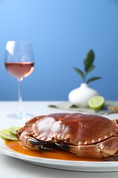Photo of Delicious crab with sauce and lime on white table against light blue background, closeup