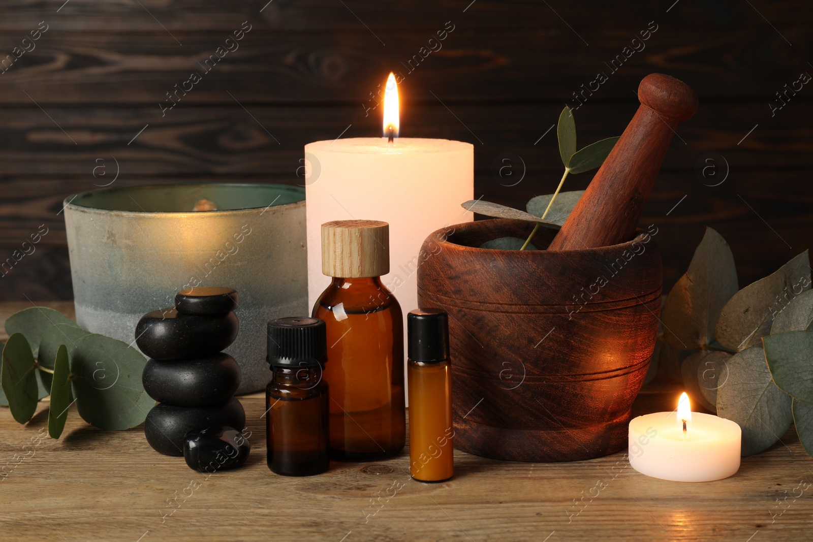 Photo of Aromatherapy. Scented candles, bottles, eucalyptus branches and mortar on wooden table