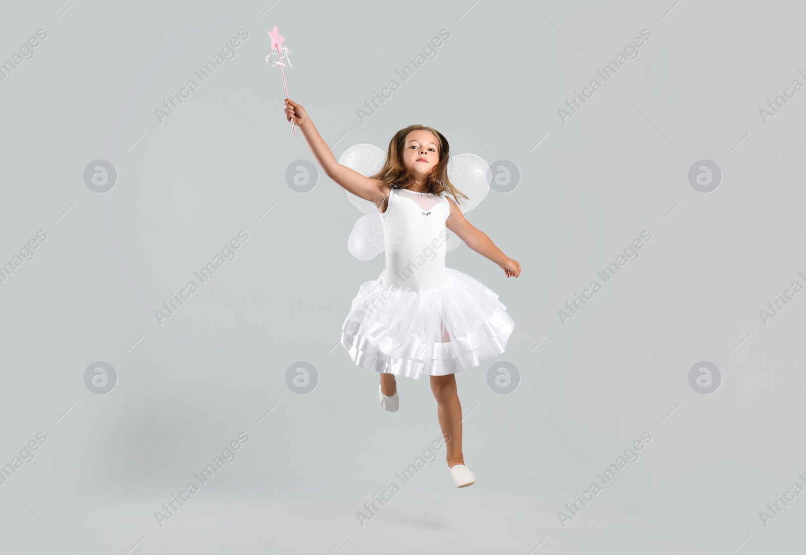 Photo of Cute little girl in fairy costume with wings and magic wand on light background