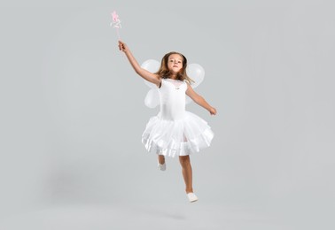 Photo of Cute little girl in fairy costume with wings and magic wand on light background