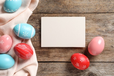 Flat lay composition of painted Easter eggs and card on wooden table, space for text