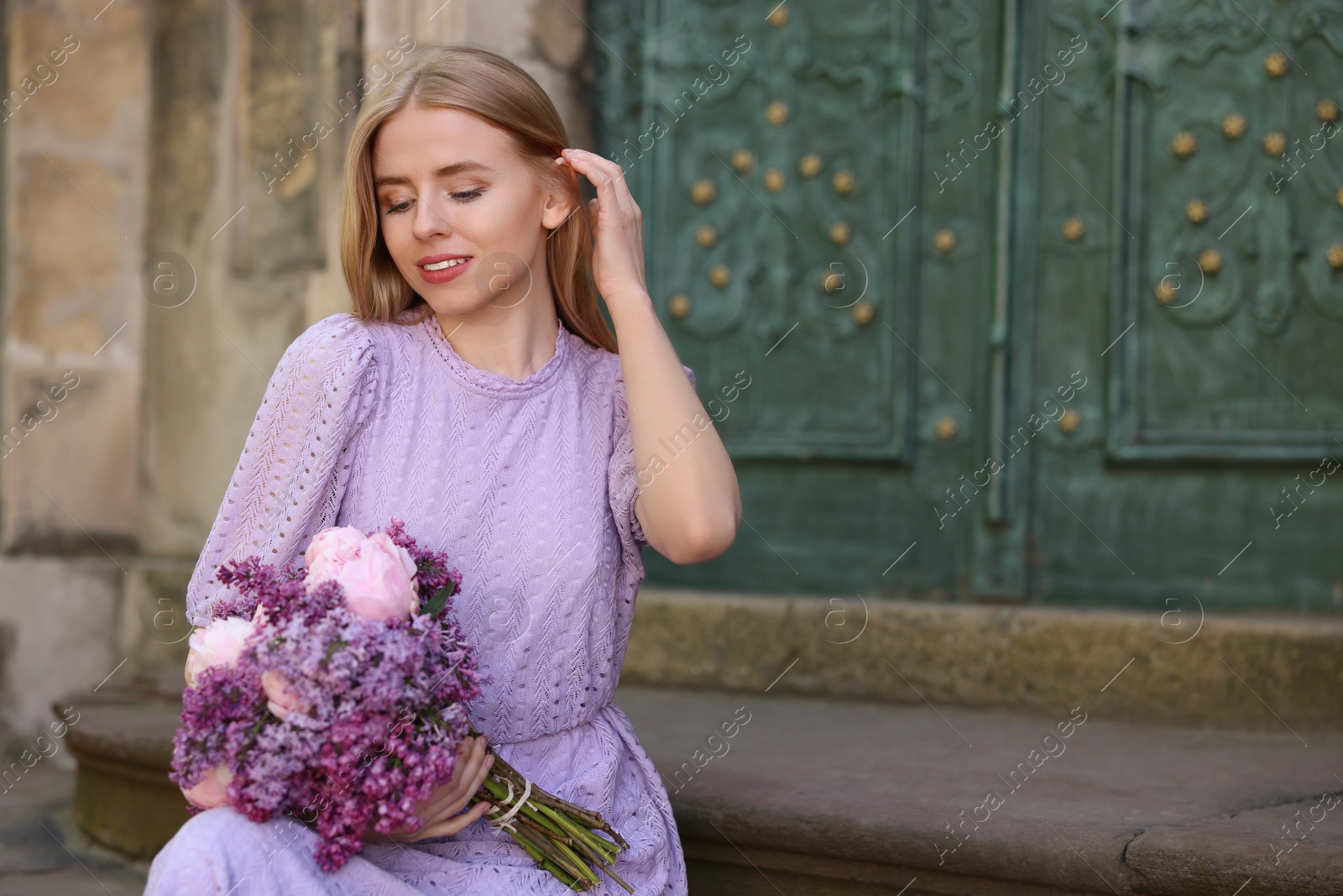 Photo of Beautiful woman with bouquet of spring flowers near building outdoors, space for text