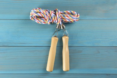 Skipping rope on light blue wooden table, top view. Sports equipment