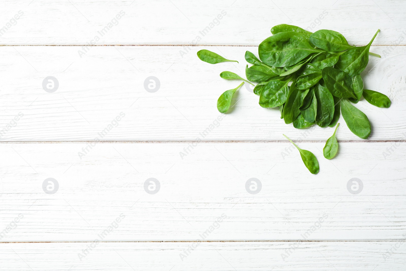 Photo of Heap of fresh green healthy spinach on white wooden table, top view. Space for text