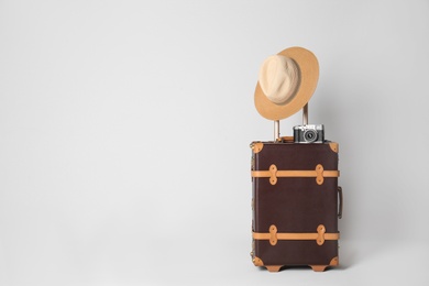 Vintage travel suitcase with hat and camera on light grey background, space for text. Summer vacation