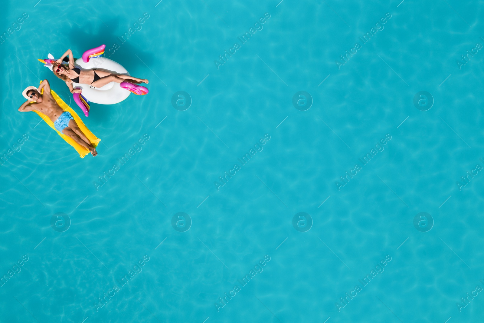 Image of Happy couple with inflatable ring and mattress in swimming pool, top view. Summer vacation