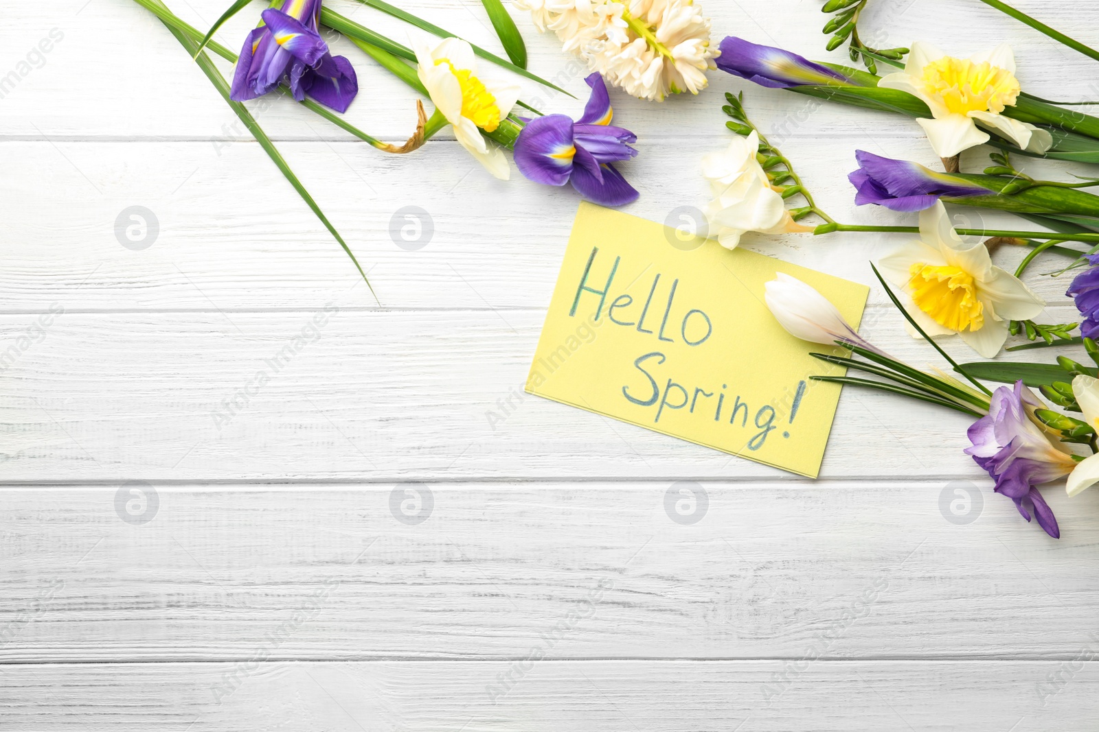 Photo of Card with words HELLO SPRING and fresh flowers on white wooden table, flat lay. Space for text