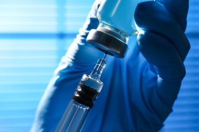 Photo of Woman filling syringe with vaccine from vial on blurred background, closeup