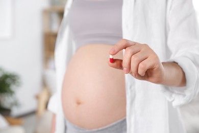 Photo of Pregnant woman holding pill at home, closeup