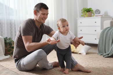 Photo of Father supporting his baby daughter while she learning to walk at home