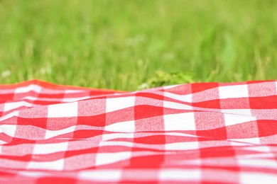 Checkered picnic tablecloth on fresh green grass, closeup