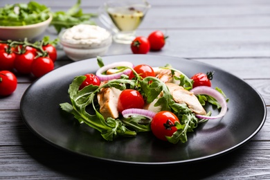 Delicious salad with chicken, vegetables and arugula on grey wooden table