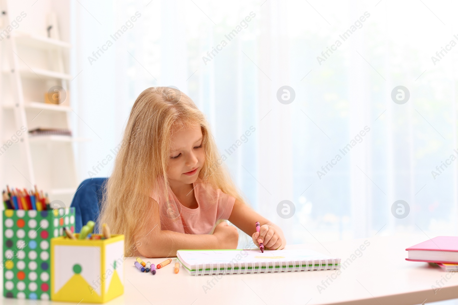 Photo of Cute little left-handed girl drawing at table in room