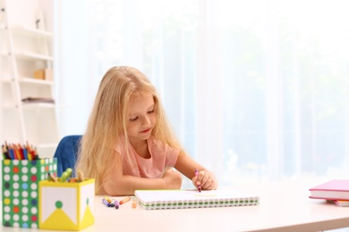 Photo of Cute little left-handed girl drawing at table in room