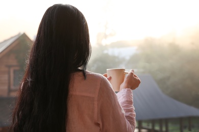 Photo of Young woman with cup of tea enjoying beautiful view in morning