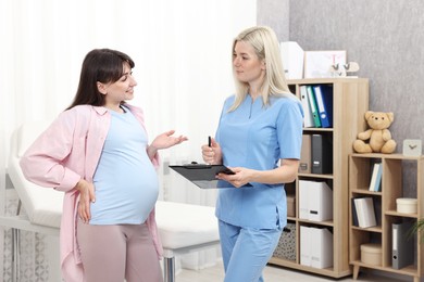 Photo of Doctor with clipboard consulting pregnant patient in clinic