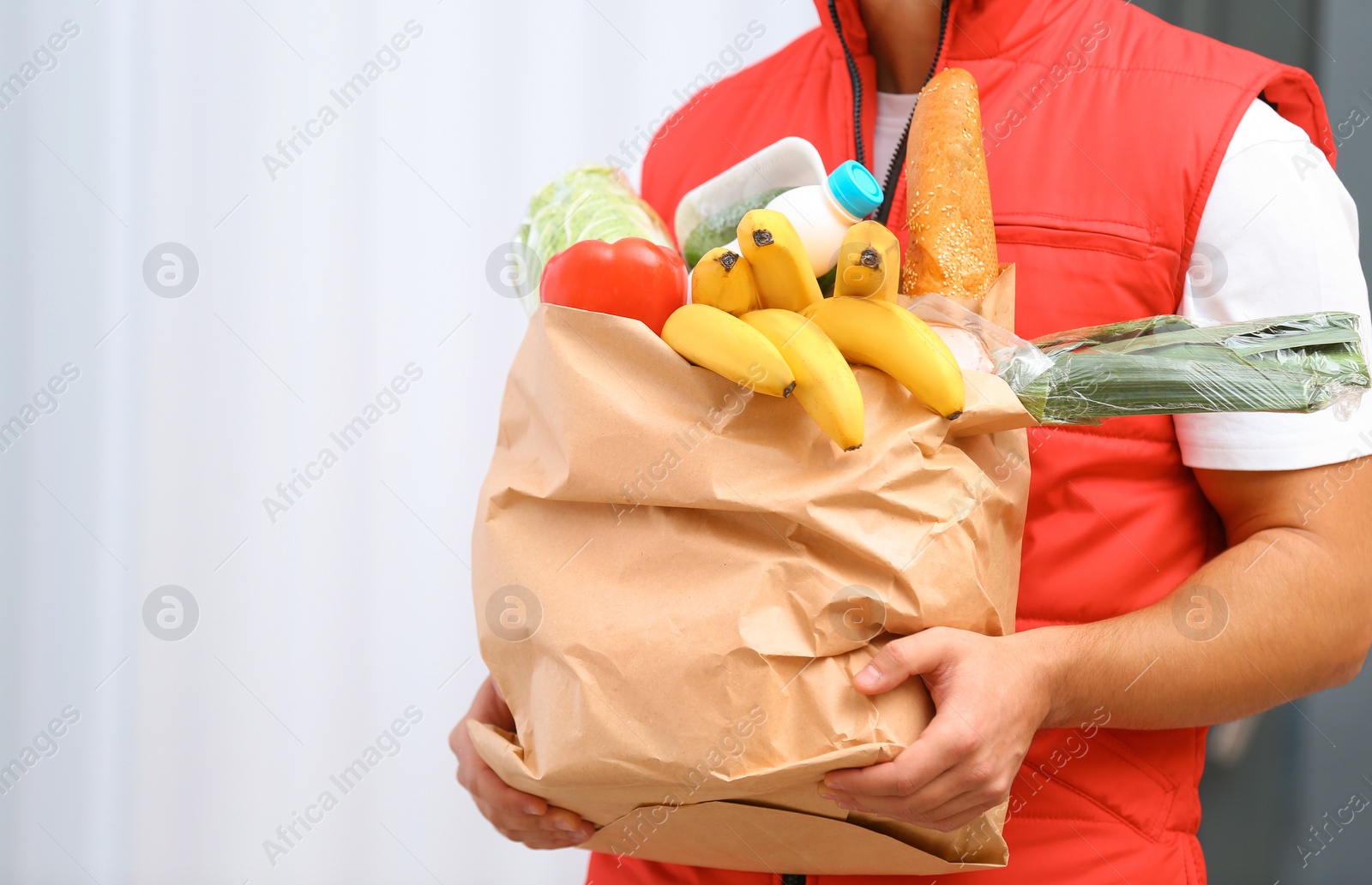 Photo of Food delivery courier holding paper bag with products indoors, closeup. Space for text