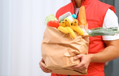 Food delivery courier holding paper bag with products indoors, closeup. Space for text