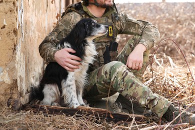 Photo of Ukrainian soldier with stray dog sitting outdoors, closeup