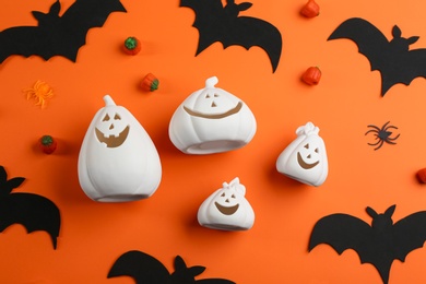 Image of White pumpkin shaped candle holders, jelly candies, decorative bats and spiders on orange background, flat lay. Halloween celebration