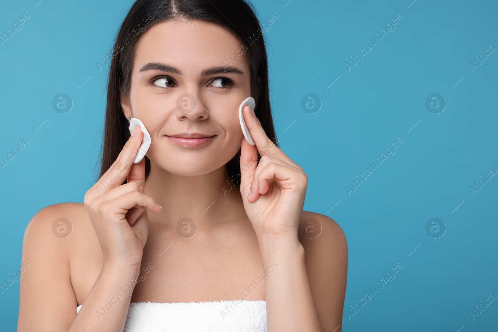 Photo of Young woman cleaning her face with cotton pads on light blue background. Space for text