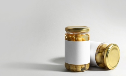 Glass jars with pickled baby corn and mushrooms on white background. Space for text