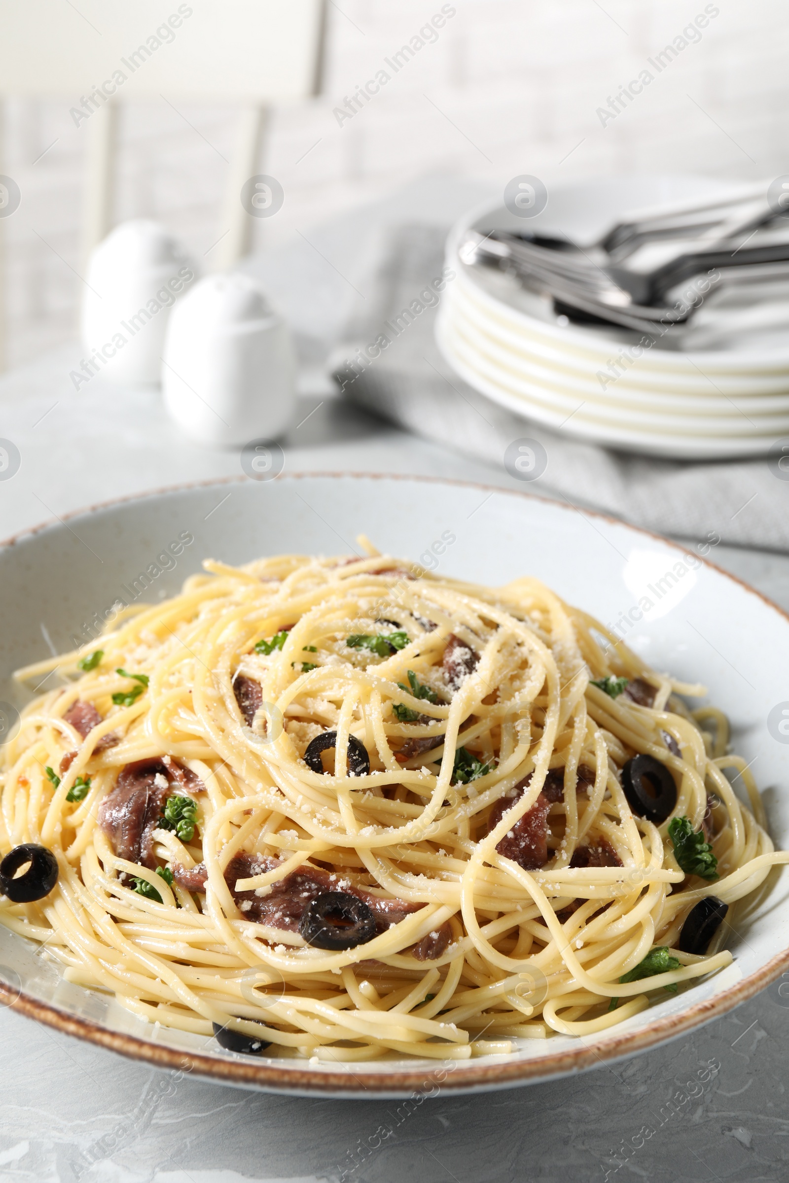 Photo of Delicious pasta with anchovies, olives and parmesan cheese served on grey marble table, closeup